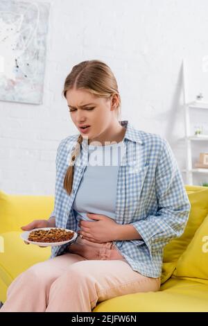 Femme malade avec une plaque de retenue des allergies avec des noix sur le canapé Banque D'Images