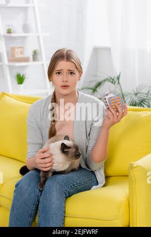 Femme bouleversée avec des ampoules à l'allergie tenant avec des pilules et siamese chat sur la table Banque D'Images