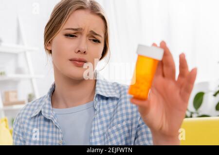 Triste femme avec l'allergie tenant bocal avec des pilules sur flou premier plan Banque D'Images