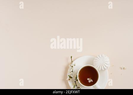 Concept de ressort. Tasse de thé noir du matin avec bonbons guimauves sur fond beige avec branche de pommier en fleur avec espace de copie Banque D'Images