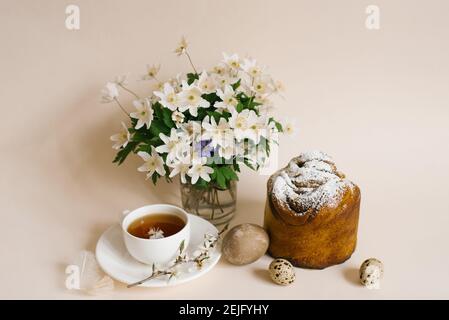 Gâteau de Pâques à l'intérieur. Faites de la spécialité avec des raisins secs, des fruits confits et une saupoudré de sucre. Gâteau fait maison. Oeufs, une tasse de thé et fleurs de printemps dans un v Banque D'Images