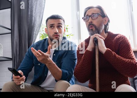 jeune homme hispanique pointant de la main tout en regardant la télévision à proximité père émerveillé Banque D'Images