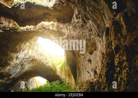 Grotte de Devetashka en Bulgarie - attraction naturelle. De hautes arches d'une immense grotte en pierre avec des trous ronds au sommet, une route touristique avec une clôture à l'intérieur du Banque D'Images