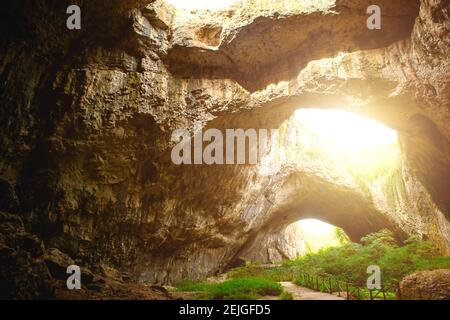 Grotte de Devetashka en Bulgarie - attraction naturelle. De hautes arches d'une immense grotte en pierre avec des trous ronds au sommet, une route touristique avec une clôture à l'intérieur du Banque D'Images