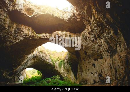 Grotte de Devetashka en Bulgarie - attraction naturelle. De hautes arches d'une immense grotte en pierre avec des trous ronds au sommet, une route touristique avec une clôture à l'intérieur du Banque D'Images
