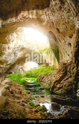 Grotte de Devetashka en Bulgarie - attraction naturelle. De hautes arches d'une immense grotte en pierre avec des trous ronds au sommet, une route touristique avec une clôture à l'intérieur du Banque D'Images