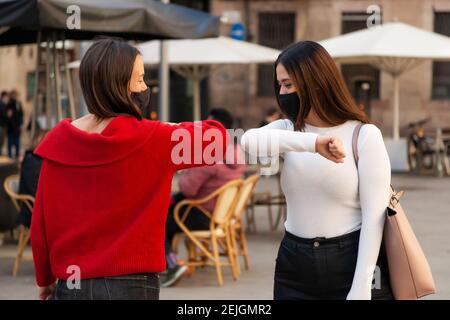 Deux femmes amies avec des masques protecteurs se saluaient mutuellement avec une bosse de coude pendant une pandémie de coronavirus. Concept: Distanciation sociale et relations Banque D'Images