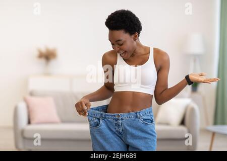 Femme africaine fine excitée portant un pantalon surdimensionné après perte de poids en intérieur Banque D'Images