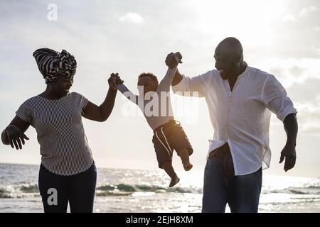Parents africains et petit fils s'amusant sur la plage Au coucher du soleil - concept de famille et d'amour - principal concentrez-vous sur le corps de votre enfant