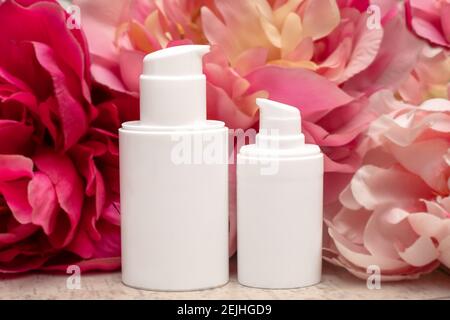 Ensemble cosmétique de deux récipients en plastique de bouteilles avec distributeur sur fond de fleurs de pivoine rose. Design élégant. Concept de soins organiques de la peau. Faux Banque D'Images