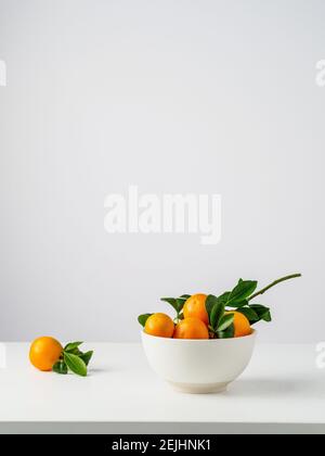 Bol blanc de clémentines fraîches avec des feuilles vertes sur la table blanche et le fond. Copier l'espace. Banque D'Images