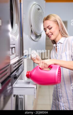 la femme verse un détergent gras en bouteille rose dans le compartiment de la machine à laver, dans la maison à laver Banque D'Images
