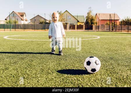 Mignon petit garçon jouant au football avec le ballon à l'extérieur sur le football champ Banque D'Images