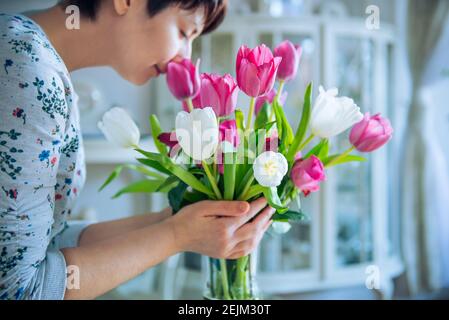 Gros plan bouquet de tulipes roses et blanches dans un vase et femme floue appréciant des fleurs odorat avec des yeux fermés dans un intérieur clair. Vie lente Banque D'Images