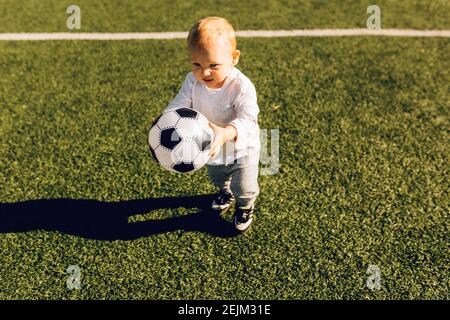 Mignon petit garçon jouant au football avec le ballon à l'extérieur sur le football champ Banque D'Images