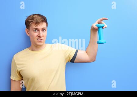 sportif tenant une petite haltère, il n'est pas difficile pour lui de soulever. isolé fond bleu. studio portrait de caucasien gars dans un t-shirt décontracté. Banque D'Images