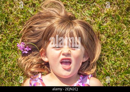 Défi Flower Girl lance un tantrum allongé dans un pré à l'extérieur avec l'attitude donne aux parents un temps difficile et est grincheux et peu coopératif parce qu'elle le fait Banque D'Images