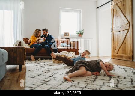 Les frères et sœurs s'amusent dans la salle de séjour. Les parents s'assoient sur un canapé avec bébé Banque D'Images