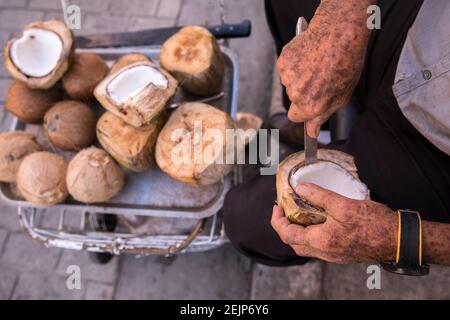 Les mains du vieil homme coupent la viande de noix de coco à l'aide d'un couteau. Banque D'Images