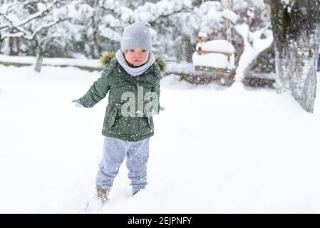 Syndrome de Down le jeune garçon jette des flocons de neige de ses mains. Flou. Un garçon handicapé apprécie le temps hivernal glacial et la neige. L'hiver s'amuser dans la cour. F Banque D'Images