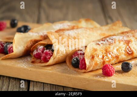 Crêpes fourrées de baies fraîches sur une planche en bois gros plan. Banque D'Images