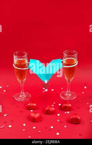 Deux vases à champagne, bonbons et masque médical Valentin sur fond rouge. 14 février 2021. Date romantique. Concept Saint Valentin. Banque D'Images