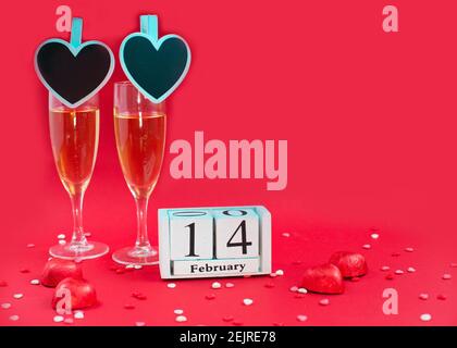 Calendrier en bois avec date du 14 février, bonbons et deux verres de champagne sur fond rouge. Date romantique. Concept Saint Valentin. Banque D'Images