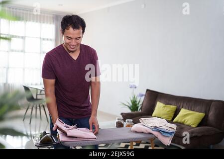 Photo d'un mari responsable ou d'un homme célibataire occupé par le travail à la maison, irroira sa chemise le matin sur le bureau de repassage avant le travail, Banque D'Images