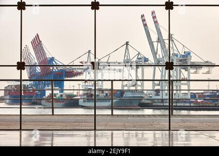 Hambourg, Allemagne. 22 février 2021. Vue à travers une façade en verre à Holzhafen d'Altona. Les navires à conteneurs et les grues du terminal à conteneurs de Tollerort sont visibles en arrière-plan. Le 23.2.2021, la conférence de presse annuelle en ligne de l'Association des armateurs allemands (VDR) aura lieu avec un bilan de 2020 et des perspectives pour 2021. Credit: Georg Wendt/dpa/Alay Live News Banque D'Images