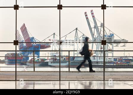 Hambourg, Allemagne. 22 février 2021. Un homme marche derrière une façade de verre le long de l'Altonaer Holzhafen. En arrière-plan, on peut voir les navires à conteneurs et les grues au terminal de conteneurs de Tollerort (effet d'essuyage dû à une longue exposition). Le 23.2.2021 la conférence de presse annuelle en ligne de l'Association des armateurs allemands (VDR) a lieu avec un bilan de 2020 et des perspectives pour 2021. Credit: Georg Wendt/dpa/Alay Live News Banque D'Images