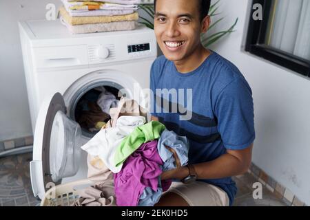 un beau mari asiatique qui met des vêtements sales un par un dans lave-linge et linge à la maison Banque D'Images