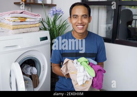 un beau mari asiatique qui met des vêtements sales un par un dans lave-linge et linge à la maison Banque D'Images