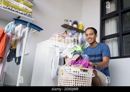 un beau mari asiatique qui met des vêtements sales un par un dans lave-linge et linge à la maison Banque D'Images