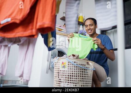 un beau mari asiatique qui met des vêtements sales un par un dans lave-linge et linge à la maison Banque D'Images