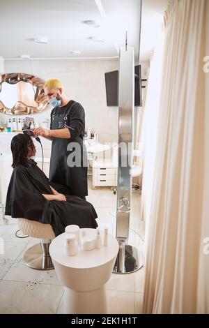 Un styliste concentré sèche les cheveux de ses clients à l'aide d'une brosse plate Banque D'Images