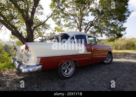 HOLGUIN, CUBA - 18 FÉVRIER; 2020 voiture rouge et blanche classique sur la piste de terre avec arbre en arrière-plan Banque D'Images