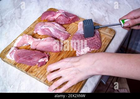 une femme hache du porc cru sur une planche à découper avec un marteau à hacher la viande Banque D'Images