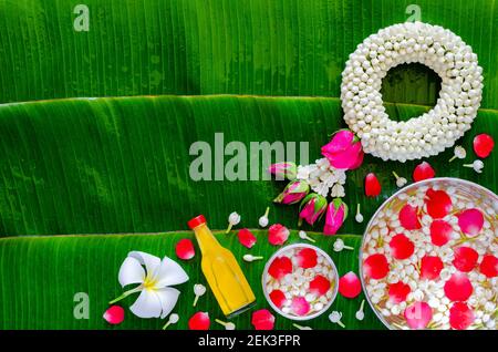 Fond du festival Songkran avec guirlande de jasmin, fleurs dans des bols d'eau et eau parfumée pour la bénédiction sur fond humide de feuilles de banane. Banque D'Images