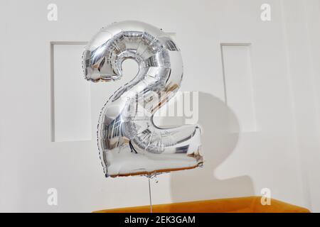 Ballon argenté en forme de numéro deux pendant l'anniversaire célébration contre le mur blanc Banque D'Images