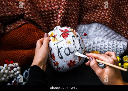 BRICOLAGE. Faites-le vous-même. Une femme peint des décorations d'action de grâce sur la citrouille d'orange pour Halloween. Récolte d'automne. Chandail maison confortable. Pinceau Banque D'Images