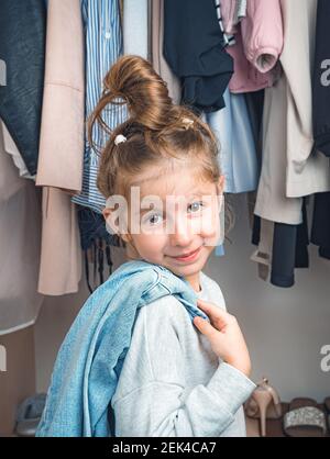 Une petite fille mignonne sourit sur le fond des vêtements sur les cintres dans le placard. Vue latérale. Banque D'Images