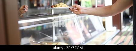 L'homme se tient derrière le comptoir de la nourriture prête à l'emploi dans la salle à manger et tient l'assiette avec le déjeuner dans sa main. Banque D'Images