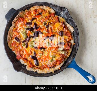 Une pizza maison grillée avec pâte de tomate, chorizo, olive, cheddar et garniture de piment dans une poêle bleue le Creuset sur un plan de travail en marbre Banque D'Images