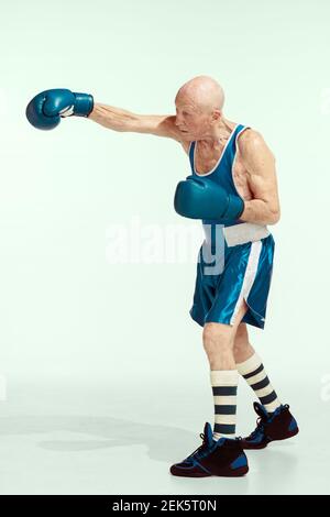 Poinçon. Homme senior portant des vêtements de boxe sur fond de studio. Le modèle mâle caucasien en grande forme reste actif et sportif. Concept de sport, d'activité, de mouvement, de bien-être. CopySpace, publicité. Banque D'Images