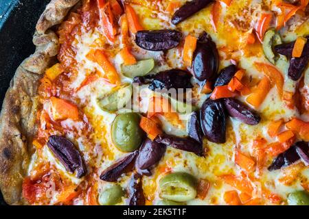 Vue rapprochée d'une pizza maison grillée avec pâte de tomate, chorizo, olive, cheddar et garniture de piment dans une poêle bleue le Creuset Banque D'Images