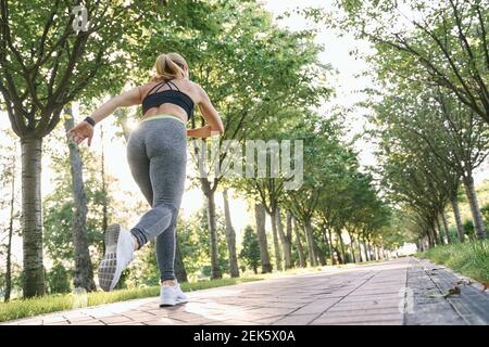 Continuez à bouger. Vue arrière de la femme sportive dans les vêtements de sport commençant à courir pendant l'entraînement dans le parc vert le jour ensoleillé Banque D'Images
