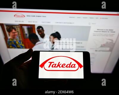 Personne tenant un smartphone avec le logo de la société pharmaceutique japonaise Takeda Limited à l'écran devant le site Web. Mise au point sur l'affichage du téléphone. Banque D'Images