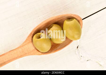 Quelques olives vertes bio piquantes et savoureuses et épicées et une cuillère en bois, sur fond de bois peint blanc naturel. Banque D'Images