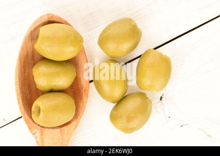 Quelques olives vertes bio piquantes et savoureuses et épicées et une cuillère en bois, sur fond de bois peint blanc naturel. Banque D'Images