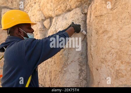 Un agent de préservation injecte un coulis liquide à base de calcaire dans les fissures des pierres vieilles de 2,000 ans du mur de l’Ouest pour les préserver et les renforcer le 23 février 2021, à Jérusalem, en Israël. Les conservateurs de l'Autorité des Antiquités d'Israël ont commencé le travail de conservation pour préparer le mur occidental pour la Pâque. Cette section du mur de soutènement du complexe du Mont du Temple est inspectée et nettoyée deux fois par an, une fois avant la Pâque et l'autre fois avant Rosh Hashanah la nouvelle année juive. Banque D'Images